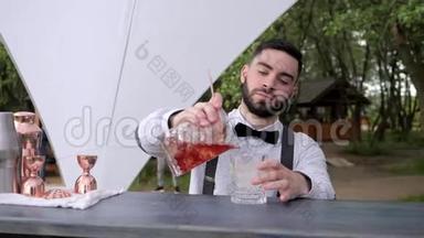 酒吧服务员将冰镇的酒倒入装有冰块的玻璃杯中，酒吧服务员在酒吧柜台准备冷却鸡尾酒，夏季咖啡厅
